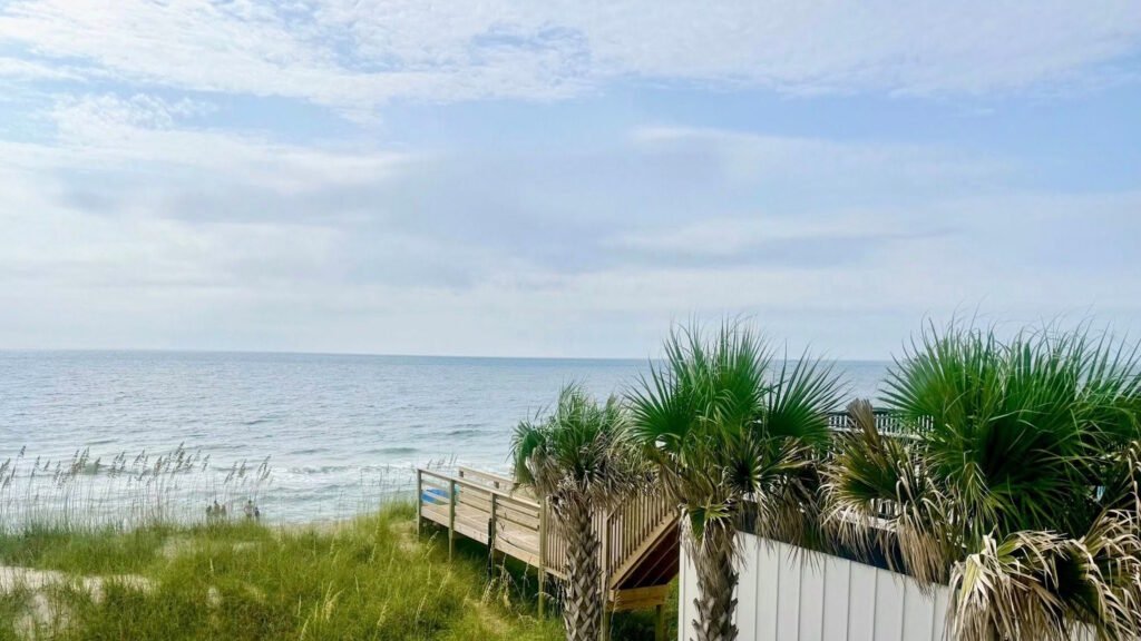 View of Kure Beach and the waves on the ocean including palm trees and a wooden walkway