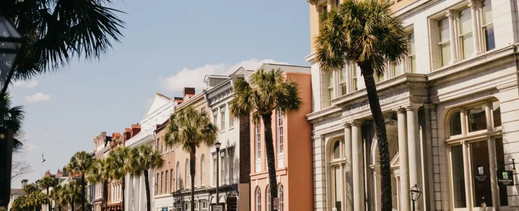 Sunny street view of historic colorful buildings and palm trees lining a downtown street in Charleston, South Carolina, with 'The Peoples Building' visible on the right.