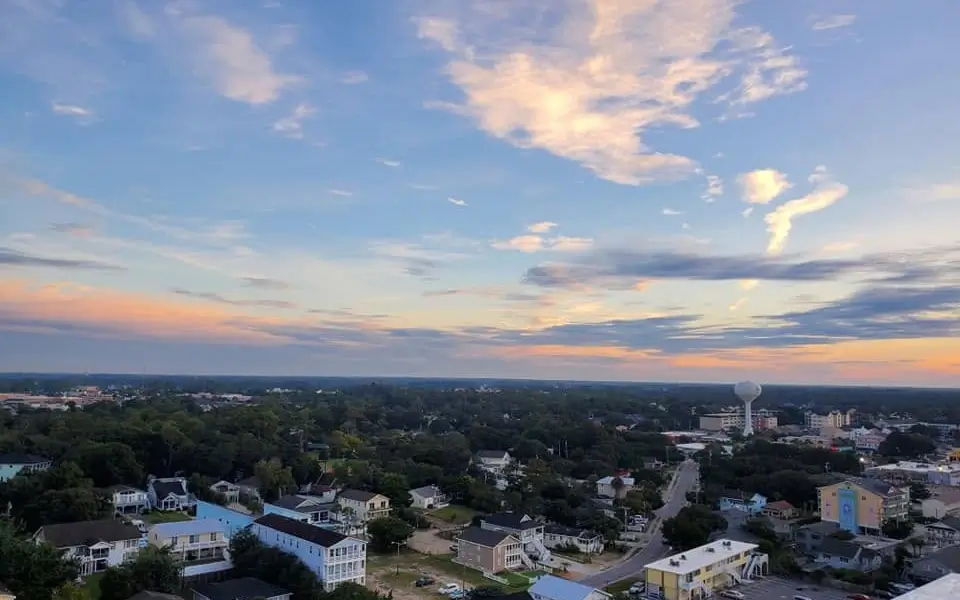 Aerial view of a residential neighborhood in Myrtle Beach, South Carolina, at sunset, with pastel-colored clouds stretching across a blue sky above homes, tree-lined streets, and a distant water tower.