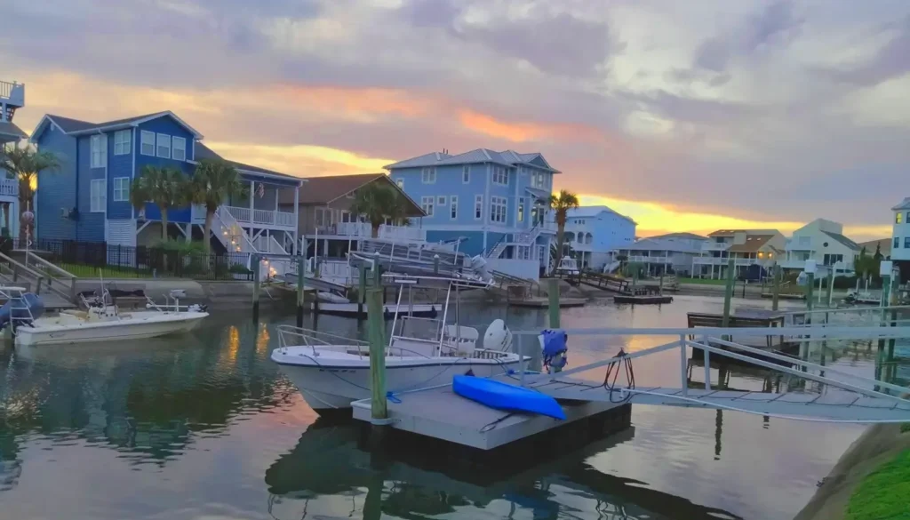Scenic sunset over a coastal canal in Ocean Isle Beach, North Carolina, featuring large beach houses, private boat docks, a small motorboat, and a blue kayak reflected in calm water.