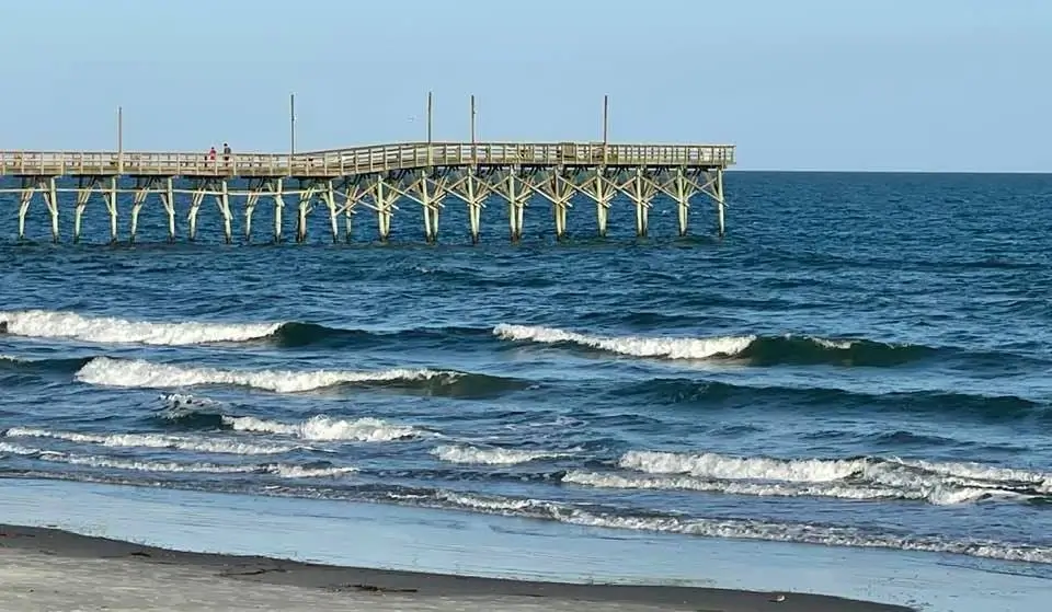 Wooden fishing pier extending into the Atlantic Ocean at Sunset Beach, NC, with rolling waves in the foreground