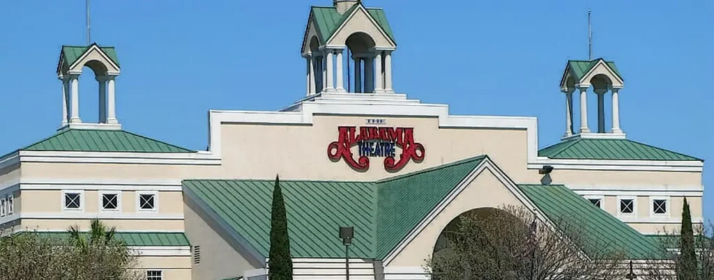 The Alabama Theatre, an iconic landmark in Myrtle Beach, featuring its distinctive green roofs and large red sign against a clear blue sky