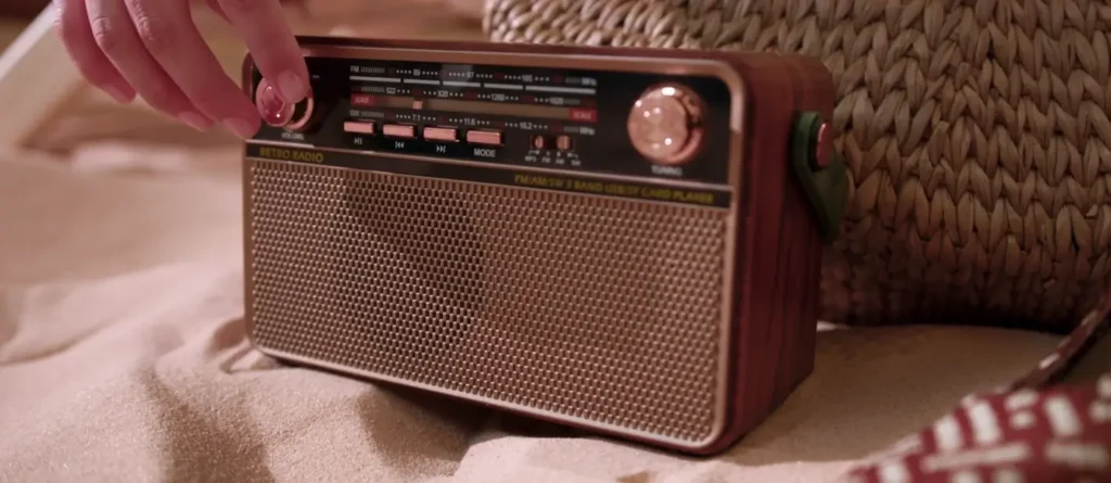A hand tuning a vintage-style wooden retro radio resting on the sand, evoking a relaxed beach atmosphere.