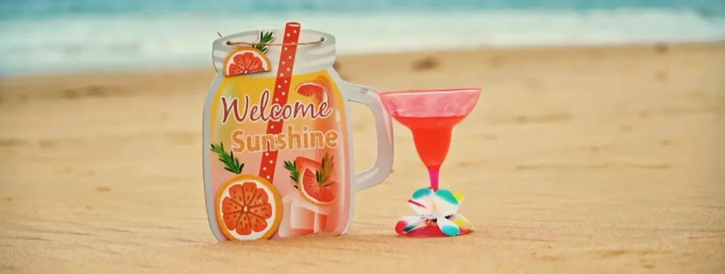 Colorful beach drink decorations on the sand, featuring a 'Welcome Sunshine' mason jar sign and a bright pink cocktail with an ocean backdrop.