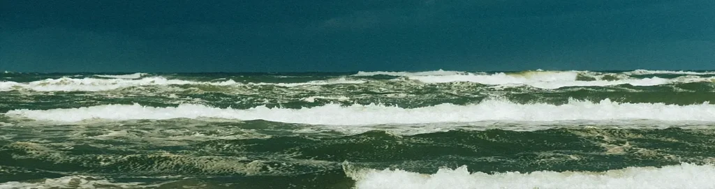 Turbulent dark green ocean with large rolling waves and whitecaps under a heavy, stormy sky.