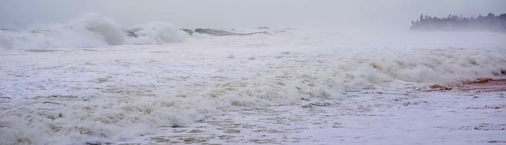 Powerful stormy waves crashing along a coastline in thick fog and mist, creating a dramatic and turbulent seascape.