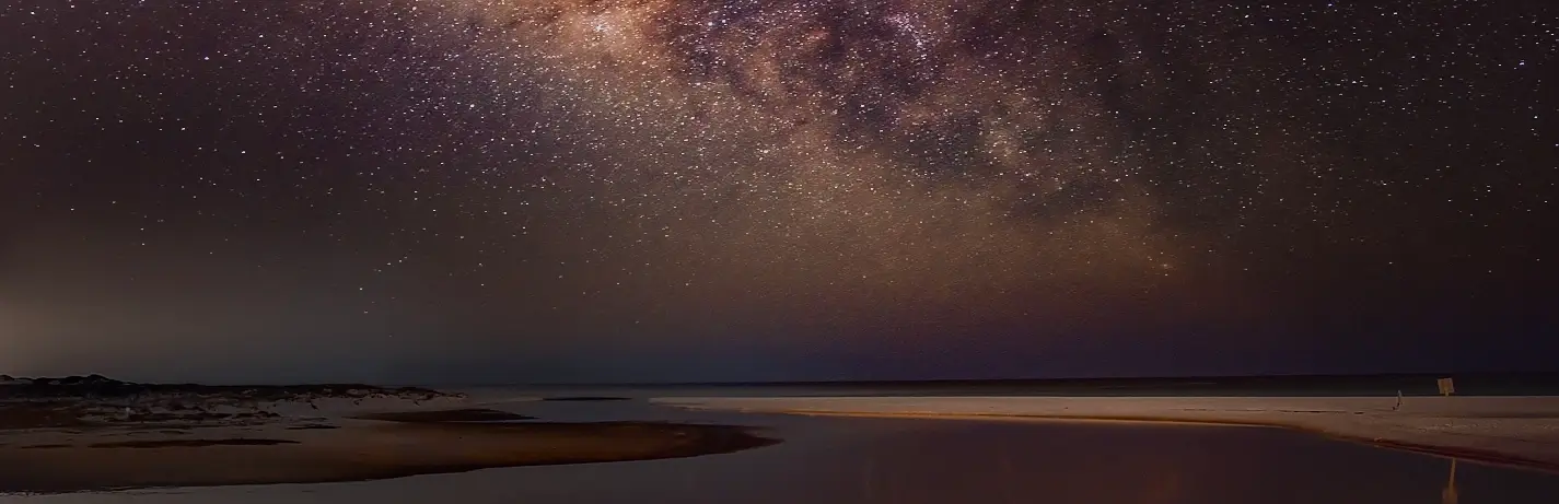 Milky Way stretching over a coastal inlet and sandbar at night