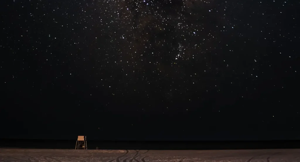 Lifeguard stand silhouetted on an empty beach beneath the Milky Way