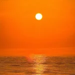 Bright orange sun setting over calm ocean water