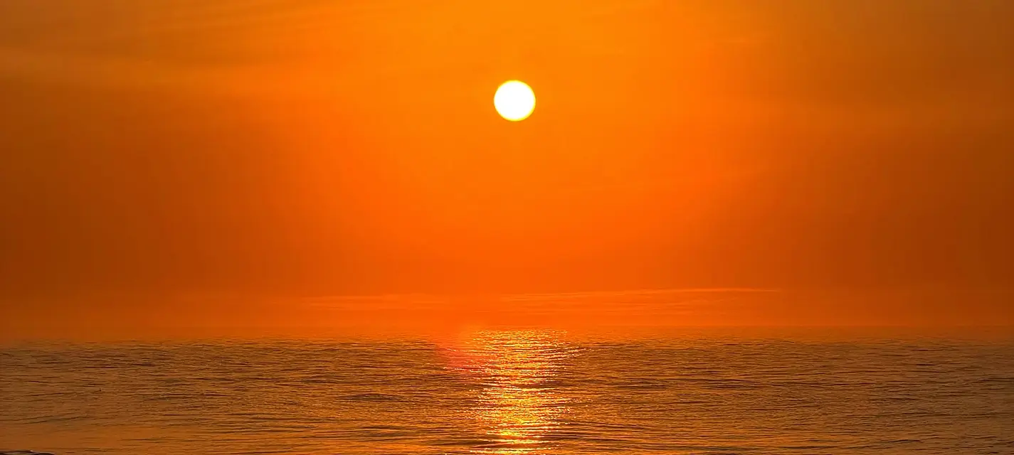 Bright orange sun setting over calm ocean water