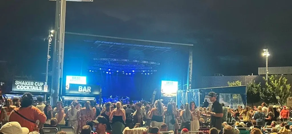 Nighttime concert at Live Oak Bank Pavilion featuring Brad Paisley on stage, with a large energetic crowd enjoying the show under blue stage lights.