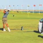 golfer swinging on a driving range lined with international flags