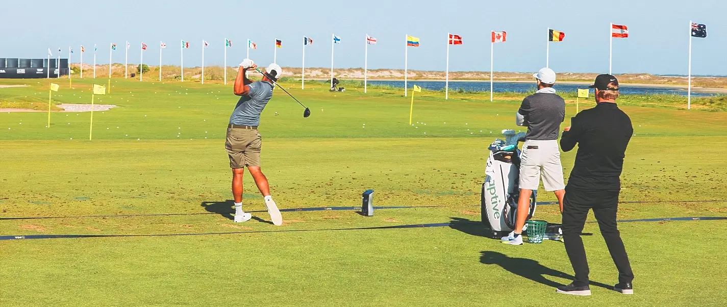 golfer swinging on a driving range lined with international flags