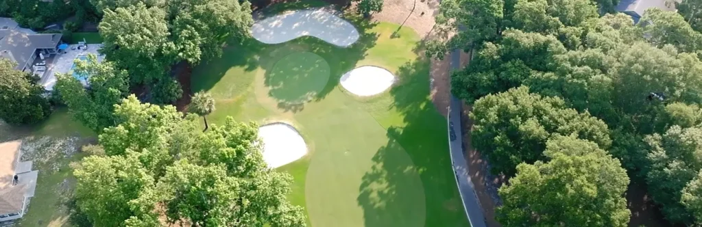 Aerial view of a golf green surrounded by trees and bunkers near a residential neighborhood