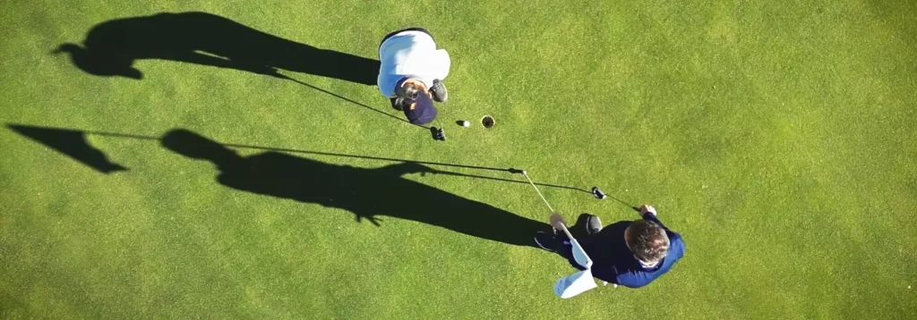 Overhead shot of two golfers putting on the green, long shadows