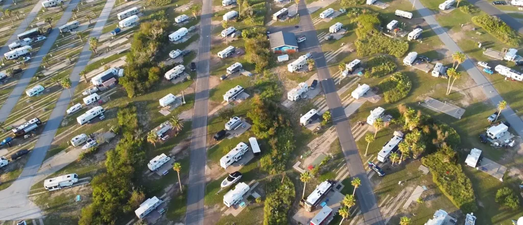 Aerial view of a large, well-organized RV resort or campground filled with dozens of RVs, palm trees, and roads, typical of popular beach RV parks.