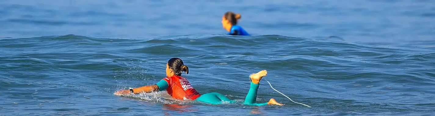 Surf contest competitors in colored jerseys paddling out through the swell