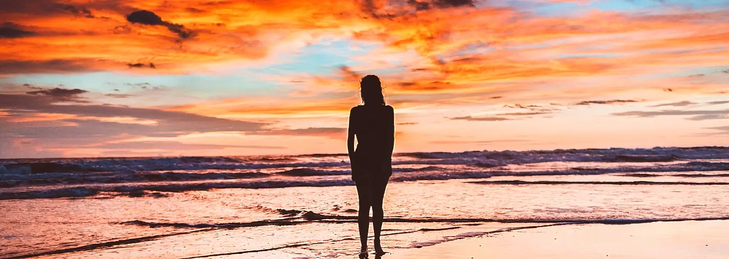 Silhouette of woman standing alone on the beach at a vivid orange sunset