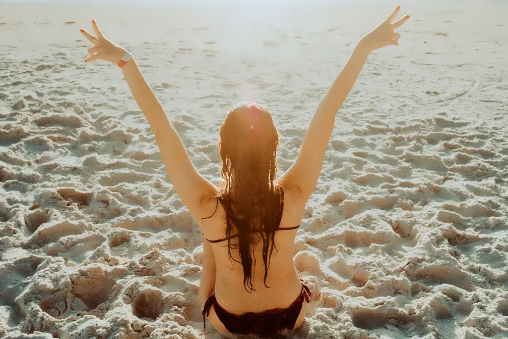Woman raising arms in celebration while sitting on a sunny beach