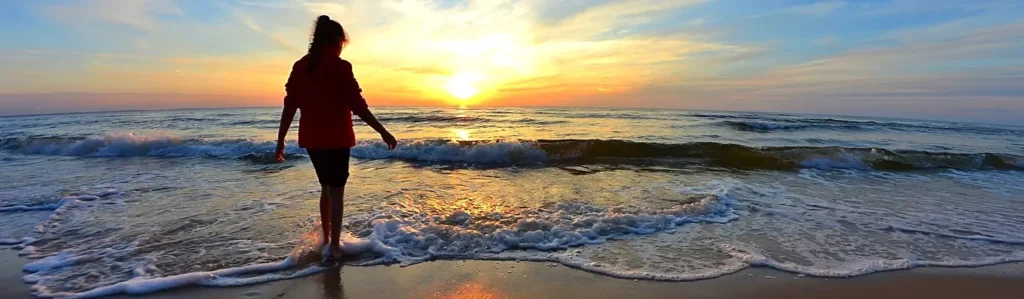 Silhouette of woman wading into ocean waves at sunset
