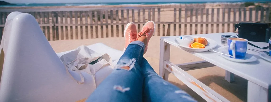 Woman's feet resting on a beachfront café railing with breakfast nearby