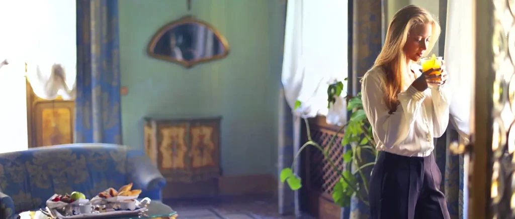 Woman drinking orange juice alone in an elegant sunlit hotel room