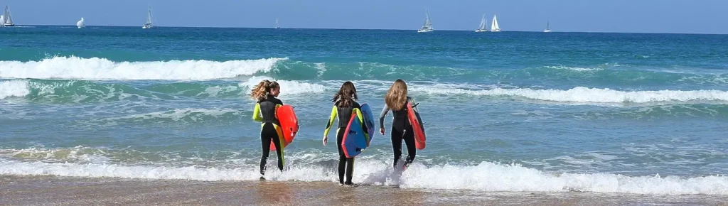 Three surfers carrying bodyboards running into the waves
