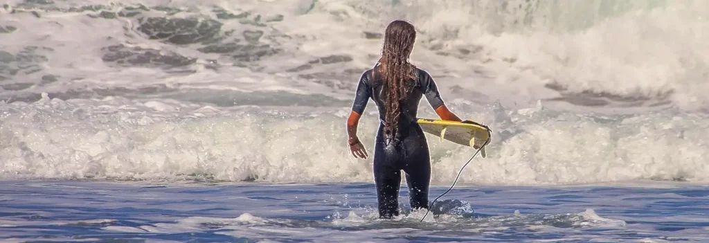 Woman wading into the surf carrying a yellow surfboard