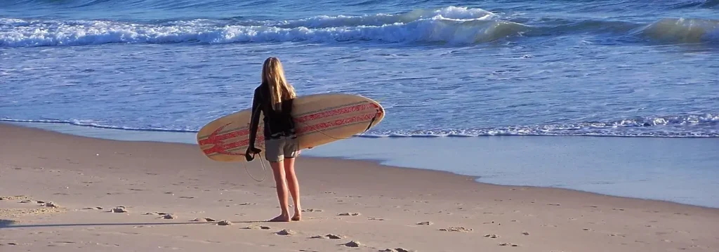 Woman standing on the beach holding a striped surfboard