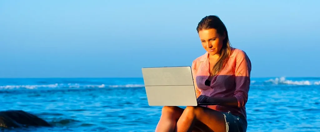 Woman working on a laptop by the ocean at golden hour