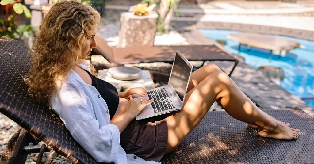 woman with curly hair working poolside on a lounge chair