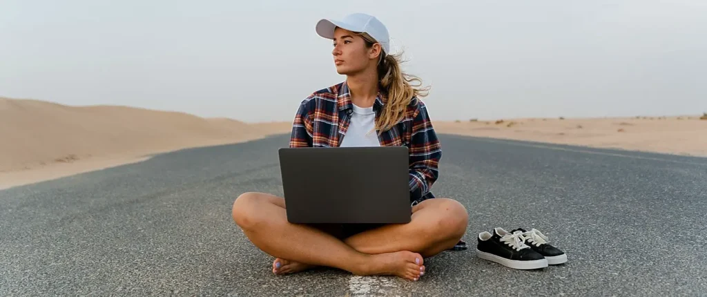Woman working on a laptop while sitting on an empty road through the dunes