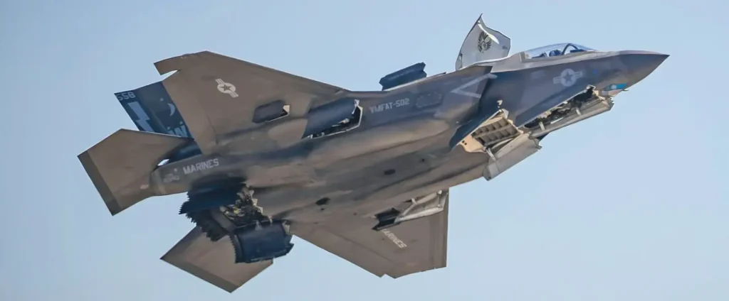 A U.S. Marine Corps F-35B Lightning II stealth fighter jet in flight, viewed from below with its cockpit canopy open and a pilot visible inside, showing VMFAT-502 squadron markings.