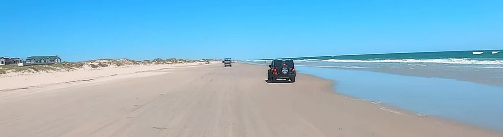 4x4 vehicles driving along the sand beach road past oceanfront homes north of Corolla