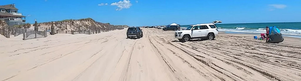 SUVs parked on the 4WD beach near Corolla vacation homes, with beachgoers unloading gear