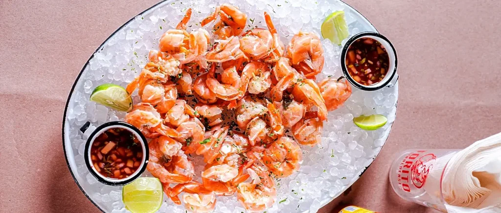 A platter of chilled peel-and-eat shrimp served with cocktail sauce and lime