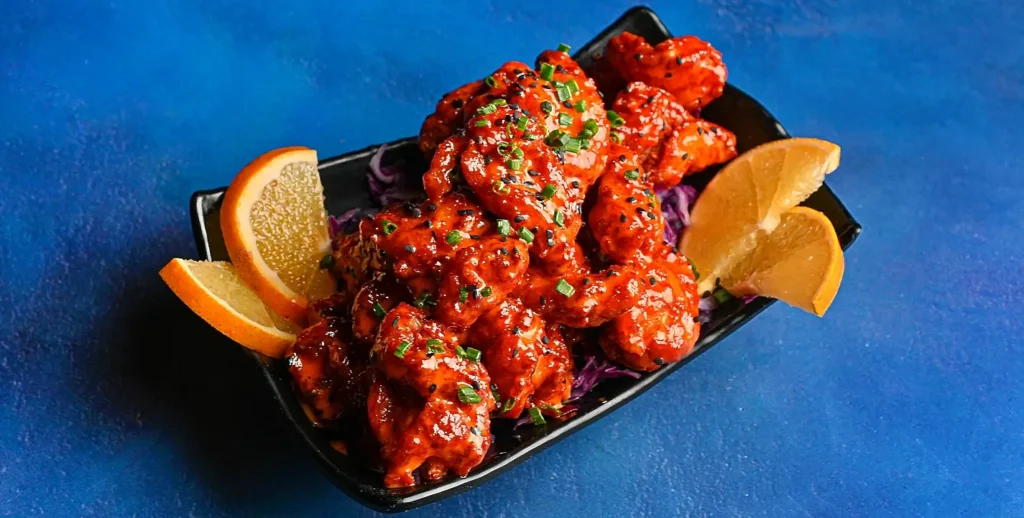 Spicy glazed shrimp garnished with sesame seeds and orange wedges