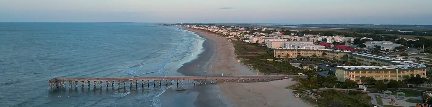 Aerial dusk view of the Folly Beach pier stretching into the Atlantic, with the town's shoreline and hotels beyond