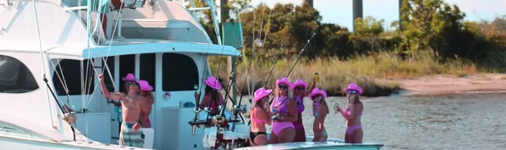 Group of women in pink hats and swimwear celebrating aboard a sportfishing boat at the dock