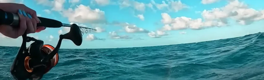 Close-up of a hand holding a fishing rod and reel with the ocean in the background