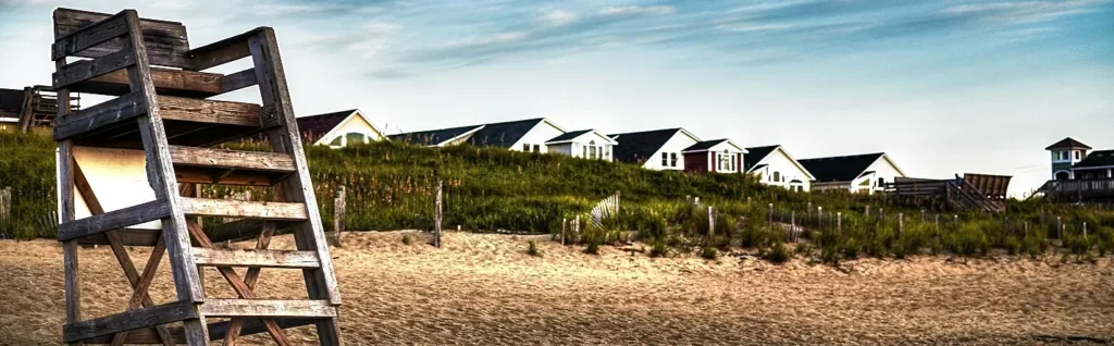Weathered wooden lifeguard chair on the beach with cottages along the dune in Kill Devil Hills, Outer Banks