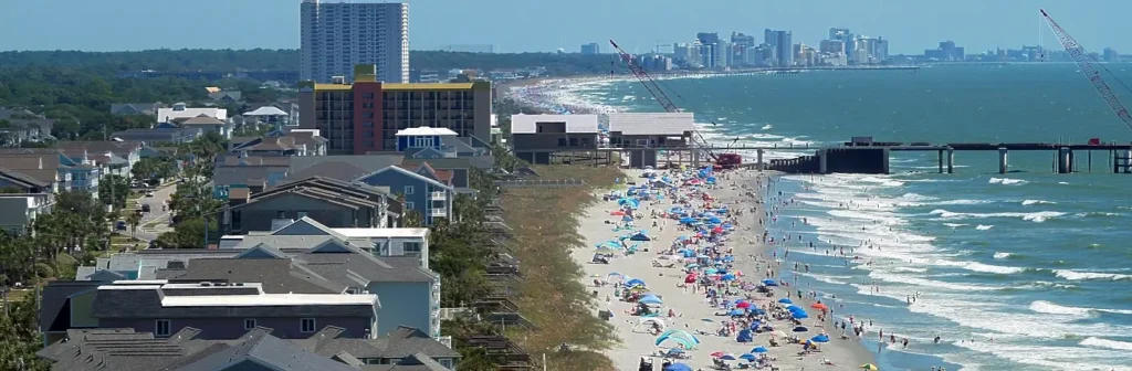 Aerial view of crowded Myrtle Beach shoreline with umbrellas, high-rises, and construction cranes