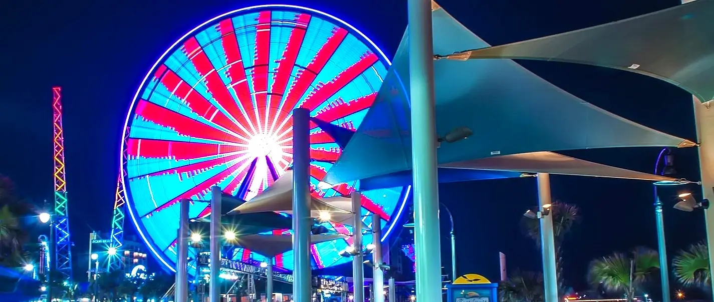 Illuminated SkyWheel Ferris wheel lit up in blue and pink at night on the Myrtle Beach Boardwalk