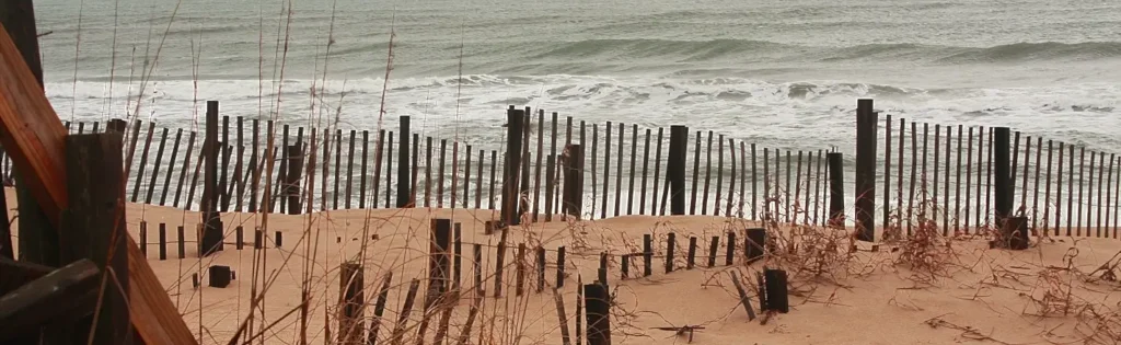 Wooden sand fence and dune grass along a quiet Outer Banks beach with rolling waves
