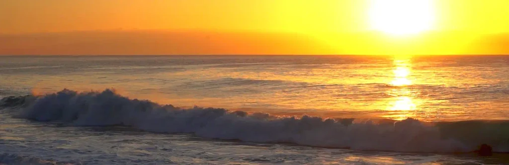 Golden sunset over the ocean with a breaking wave and bright reflection on the water, Outer Banks-style coastal scene.