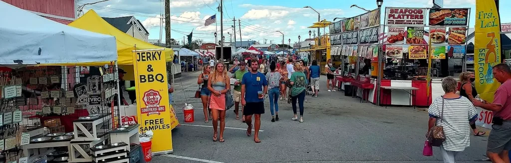 Festival-goers walking past seafood platter and BBQ jerky food stands