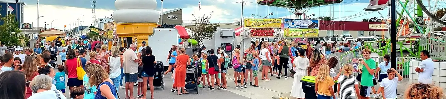 Families in line at carnival food stands with Ferris wheel at NC Seafood Festival