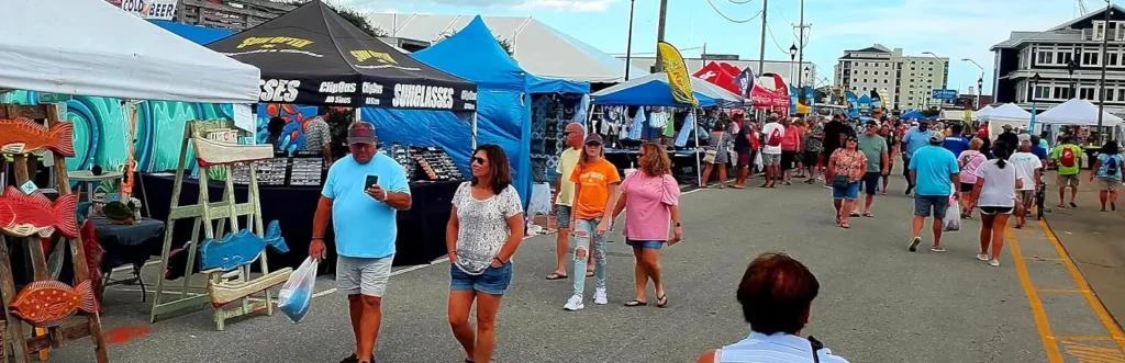 Festival-goers browsing sunglasses and souvenir vendor tents at NC Seafood Festival