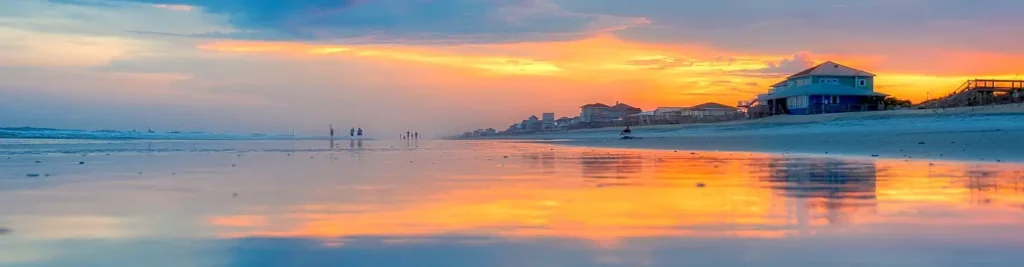 Vivid orange sunset reflecting on wet sand with beach houses along Topsail Island