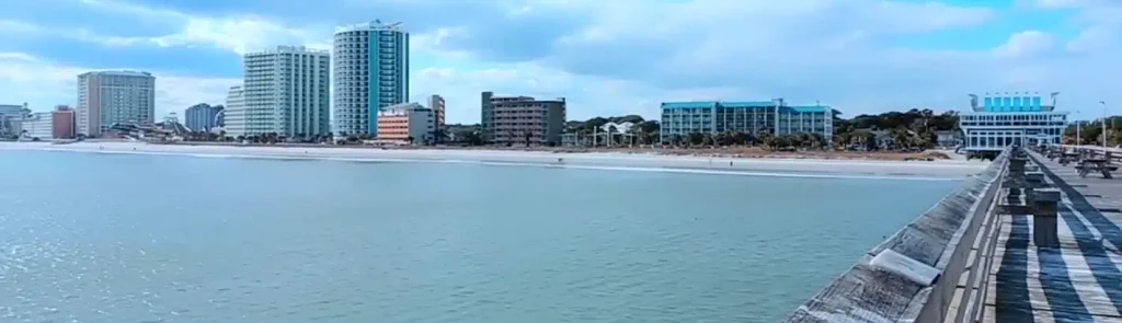 View from a pier looking toward a shoreline lined with high-rise hotels and condominiums under a partly cloudy sky.  

